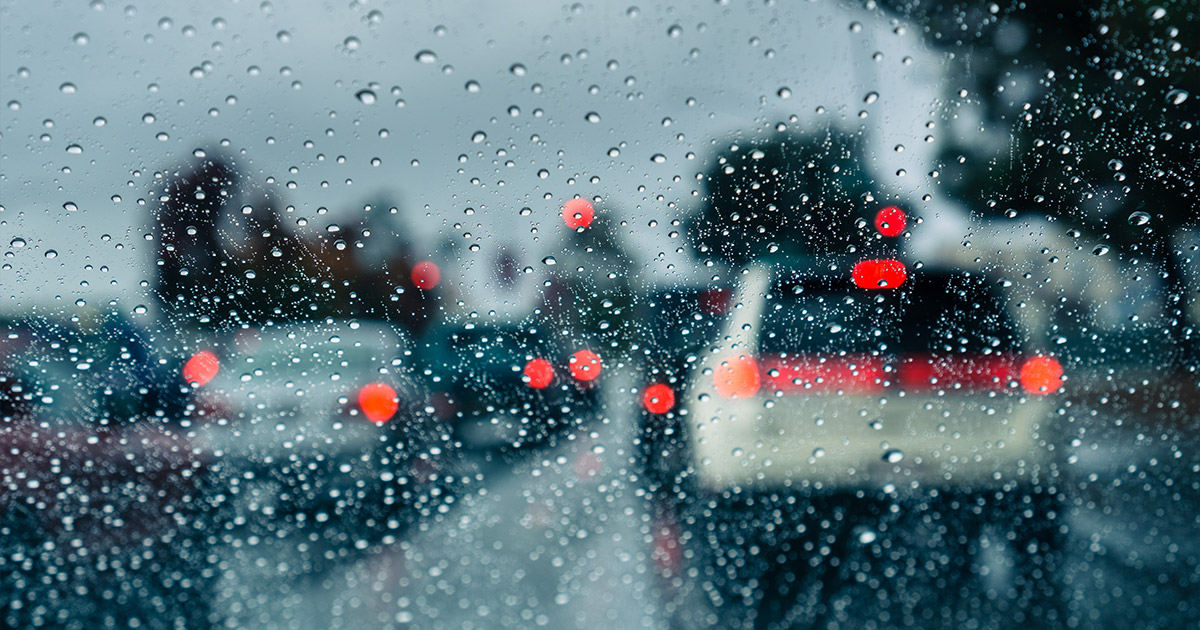 Rainy traffic scene with blurred red brake lights and water droplets on car windshield