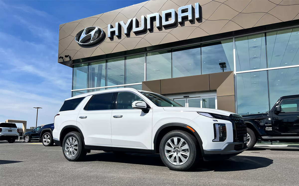 White Hyundai SUV parked in front of Hyundai dealership, modern glass building with blue sky backdrop