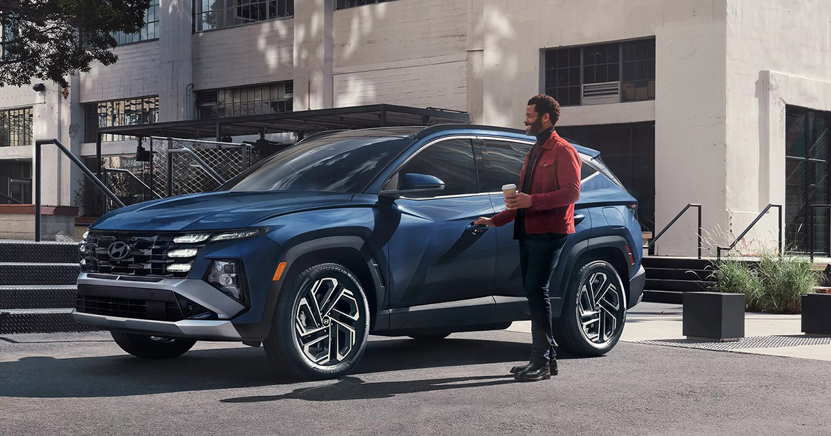 Blue Hyundai SUV parked in urban setting with person holding coffee next to modern building exterior