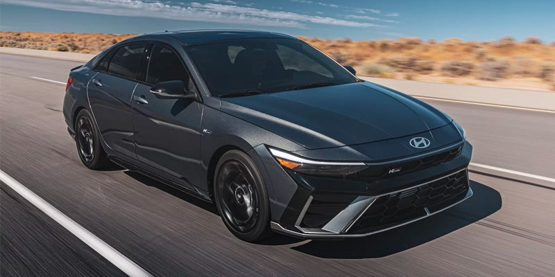 Hyundai Elantra sedan speeding right on a desert highway. Headlights are on.