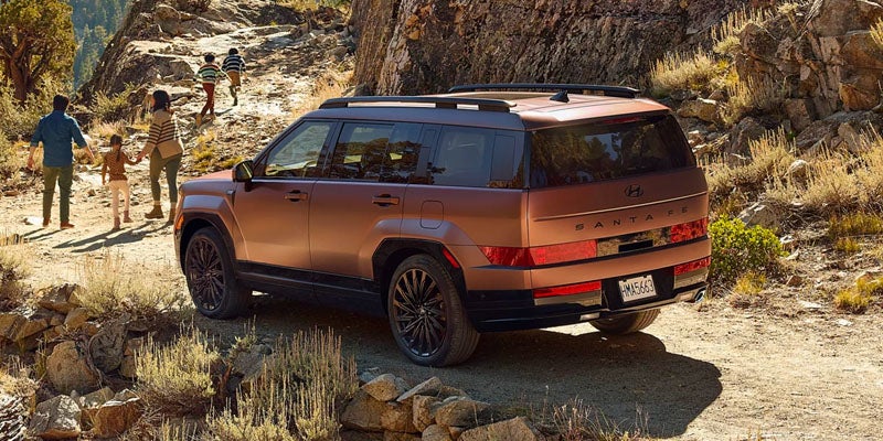 Hyundai Santa Fe SUV parked on a mountain trail, with a family strolling ahead on the rocky path.
