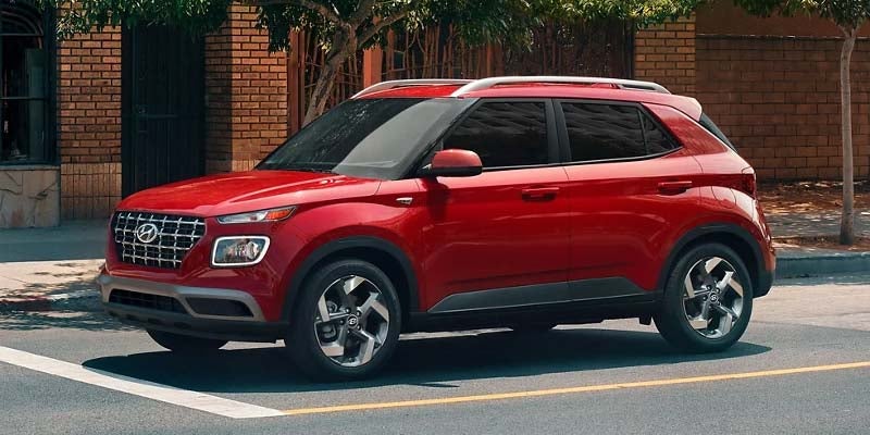 Hyundai Venue SUV with silver roof rails, parked on an asphalt street with a brick building in the background.