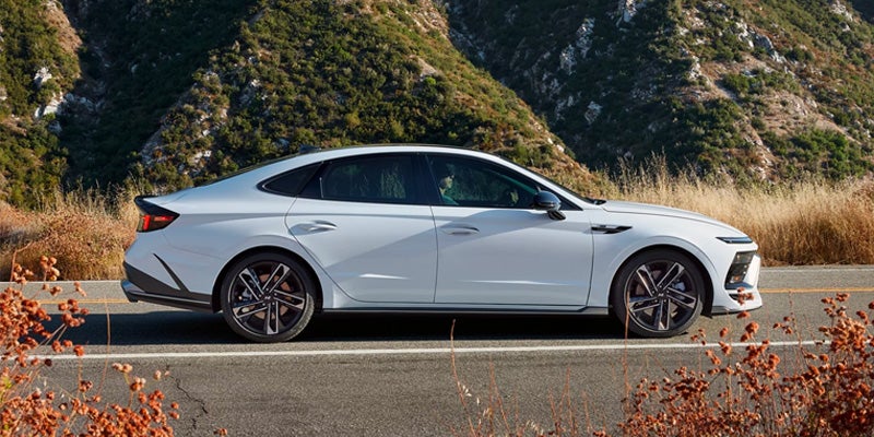 Hyundai Sonata parked sideways on a paved road with a mountain covered in green and tan foliage in background.
