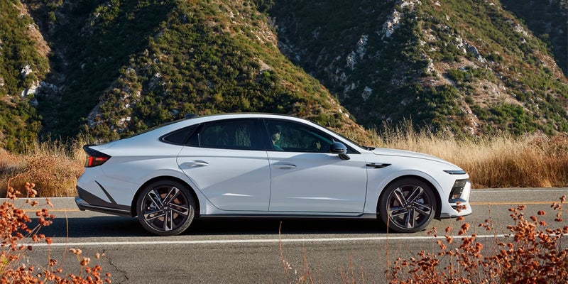 Sonata Hybrid parked on a mountain road with lush green hills and dried brown flora in the background.
